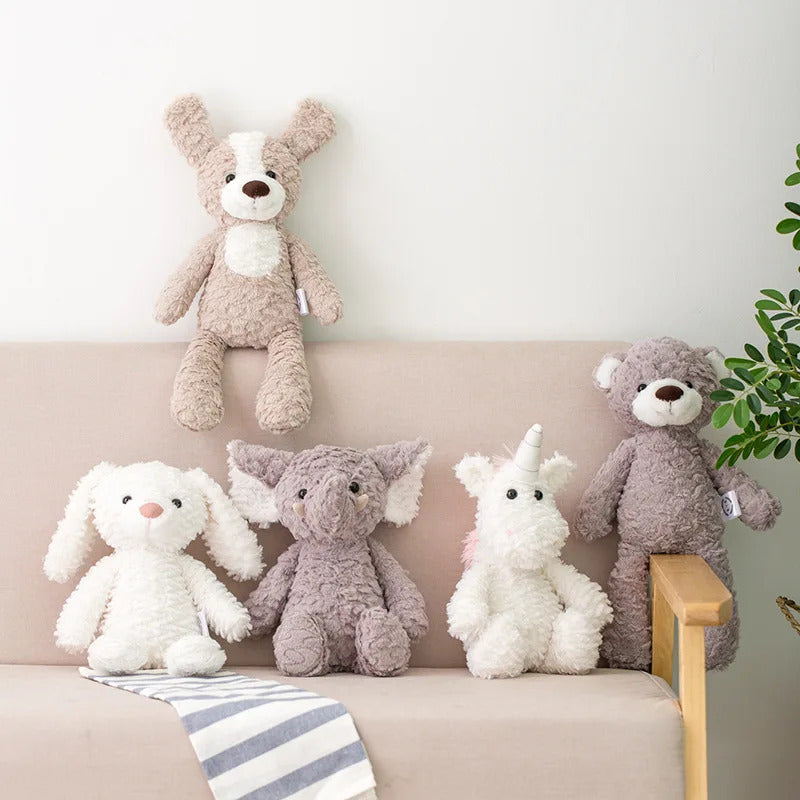 A collection of soft plush toy animals including a bunny, dinosaur, dog, frog, and owl, sitting on a shelf above a couch with a striped blanket and a potted plant in the background.