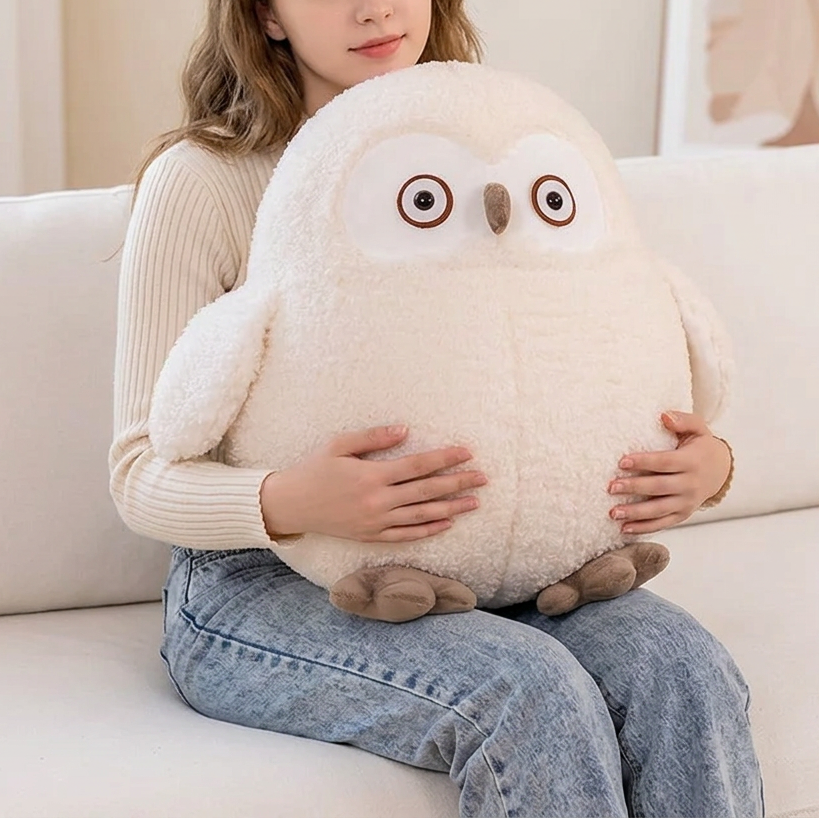 A woman sits on a cream sofa holding a large, fluffy white owl plush toy with brown eyes and feet in a brightly lit living room.