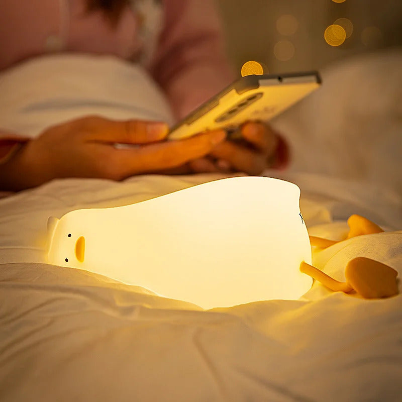 Cute silicone duck LED night light glowing softly on a white bed in a cosy bedroom setting