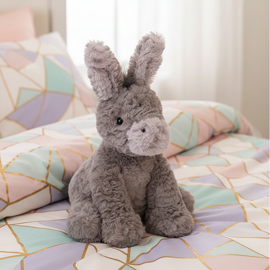 cute plush toy donkey sits upright on a pastel geometric style bedding