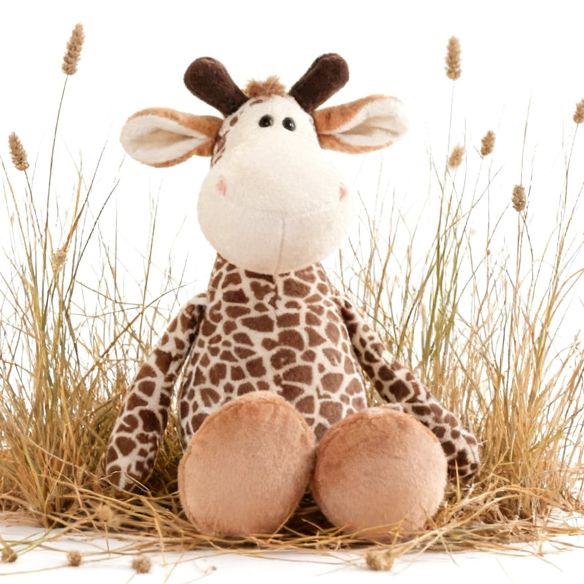 A plush giraffe toy sitting in a small arrangement of dried grass on a white background.